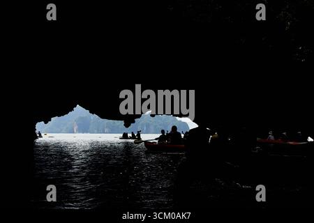 PHUKET, THAÏLANDE - 12 NOVEMBRE 2017 : silhouette de personnes faisant du kayak à travers une grotte calcaire surplombant la mer ouverte en plein jour. Banque D'Images