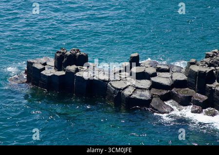 Un affleurement isolé de colonnes de basalte hexagonales émerge des vagues de Daepo Jusangjeolli. Banque D'Images