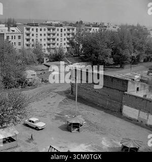 Les coulisses d'une reconstruction majeure : la vie dans les cours derrière la place centrale de Sloviansk, 1975-1976. La photo capture le mélange chaotique de la vie résidentielle, avec notamment un terrain de jeu avec des gazebos et une voiture soviétique Zhiguli, qui se poursuit au milieu du grand projet de rénovation de la ville. Cette photographie reflète le contraste saisissant entre le centre-ville cérémoniel et la vie quotidienne authentique de ses habitants, symbolisant le monde paisible et multiforme de la région du Donbass, un monde qui existait bien avant les événements tragiques de l'avenir Banque D'Images
