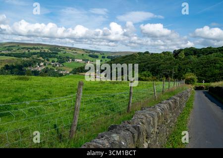 Collines verdoyantes de Pennine avec un mur de pierre sèche, une clôture en fil de fer et une voie de campagne, surplombant les vallées et les moulins lointains sous un ciel nuageux. Banque D'Images