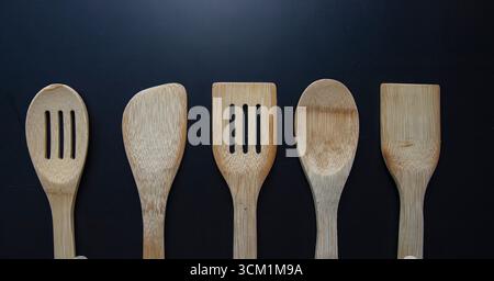 Ustensiles de cuisine en bois, y compris cuillères et spatules disposées en rangée sur un fond noir, outils de cuisine respectueux de l'environnement pour la maison et le restaurant. Banque D'Images