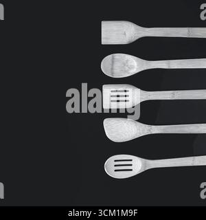 Ustensiles de cuisine en bois comprenant des cuillères et des spatules disposées en rangée sur un fond noir, des outils de cuisine naturels pour la maison et le restaurant. Banque D'Images