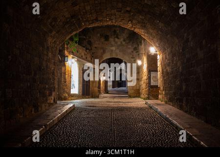 Rue pavée idyllique et vide et tunnel au site médiéval du patrimoine mondial de l'UNESCO de la vieille ville de Rhodes sur l'île de Rhodes en Grèce la nuit. Banque D'Images