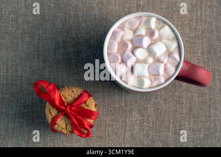 Une vue aérienne d'un seul cookie des fêtes attaché avec un ruban rouge et une tasse rouge de chocolat chaud avec des guimauves Banque D'Images