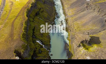 Une étroite rivière turquoise coule à travers un profond canyon en Islande, avec des murs couverts de mousse, un terrain volcanique et des cascades visibles. Banque D'Images