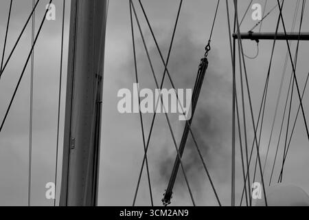 Vue monochrome des mâts et du gréement debout sur un voilier à Sail 2025 à Amsterdam, pays-Bas, avec de la fumée dérivant entre les lignes tendues. Banque D'Images