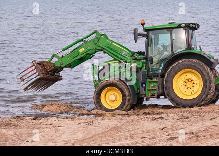 Helsingborg, Suède ; 12 août 2025 : tracteur John Deere raclant les algues du sable avec un râteau pendant le nettoyage détaillé de la plage. Banque D'Images