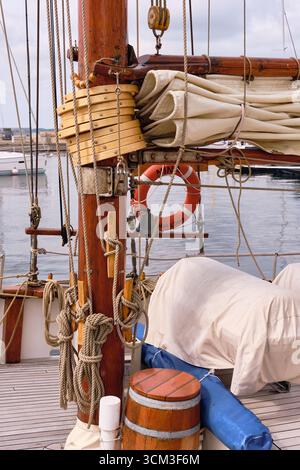 Helsingborg, Suède ; 12 août 2025 : détail du mât de yacht à voile classique en bois avec gréement, gaff et boom abaissés, voile enroulée, et cordes proprement Banque D'Images