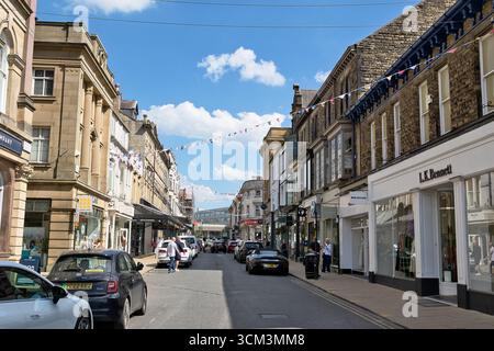Vue de rue montrant des magasins et des voitures sur une route avec des banderoles enfilées au-dessus sous un ciel bleu avec des nuages à Harrogate, Royaume-Uni. Banque D'Images