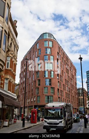 Un bâtiment en brique moderne et incurvé se dresse à côté d'un bâtiment en pierre classique dans une rue de la ville avec un camion blanc et une cabine téléphonique rouge à Londres, au Royaume-Uni. Banque D'Images
