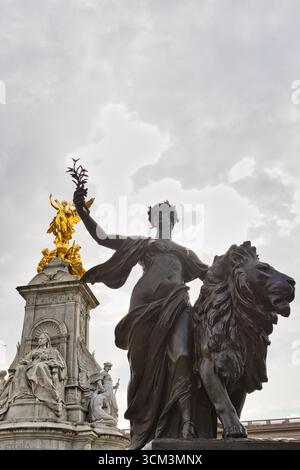 Une statue en bronze représentant une figure ailée tenant une branche se tient à côté d'un lion. En arrière-plan, une statue dorée et un monument en marbre blanc sont visibles Banque D'Images