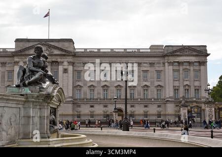 Un grand palais de pierre avec un drapeau flottant est visible derrière une statue de bronze et une fontaine. Les gens sont dispersés sur le terrain devant le palais Banque D'Images