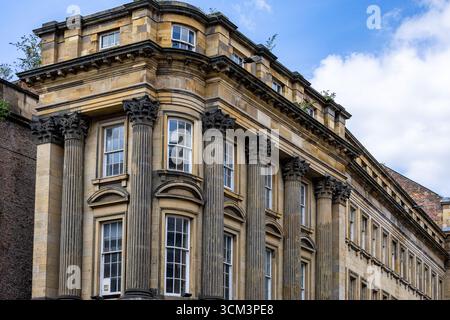 Une vue détaillée d'un grand bâtiment en pierre de plusieurs étages avec des éléments architecturaux classiques, y compris des colonnes cannelées et des chapiteaux ornés, se déroule Banque D'Images