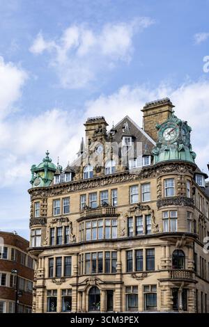 Une vue détaillée d'une grande façade de bâtiment en pierre avec des éléments architecturaux complexes, une horloge proéminente et une tourelle en dôme de cuivre contre un bl Banque D'Images
