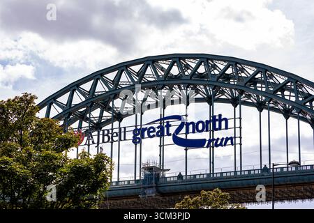 Une grande arche de pont en métal avec le lettrage bleu 'AJ Bell Great 2 North run' contre un ciel nuageux. Les arbres verts encadrent le côté gauche de l'image dans newca Banque D'Images