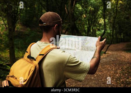 Homme avec sac à dos lisant une carte dans le parc national de Fruska Gora, Serbie. Exploration du sentier de randonnée en forêt. Vue arrière. Banque D'Images