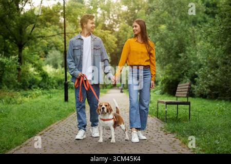 Couple marchant avec adorable chien Beagle dans le parc Banque D'Images