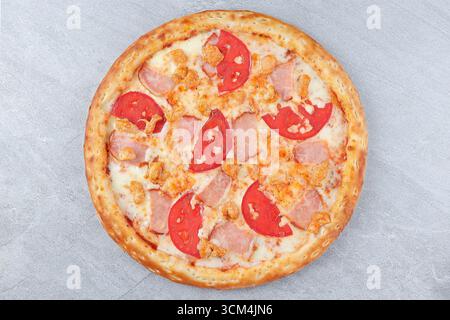 Pizza avec jambon, poulet, tranches de tomate fraîches et fromage fondu sur fond de croûte dorée sur pierre grise Banque D'Images