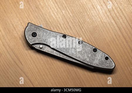 Vue détaillée d'un couteau pliant moderne en acier gris fermé avec un design élégant reposant sur un bureau en bois Banque D'Images