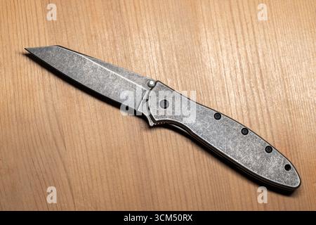 Vue détaillée d'un couteau pliant moderne en acier gris avec un design élégant reposant sur un bureau en bois, vue de dessus Banque D'Images