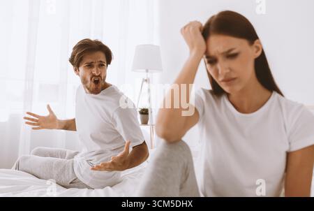 Agressif mal millénaire mari caucasien avec des cris de chaume et des essaims à offensé triste femme déprimée dans la chambre à coucher Banque D'Images