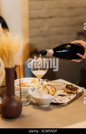 Verser du vin mousseux dans un verre lors d'un dîner confortable avec des hors-d'œuvre gastronomiques Banque D'Images