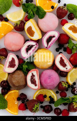 Crème glacée mochi assortie colorée avec des baies fraîches, des agrumes et de la menthe sur fond blanc Banque D'Images