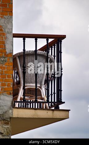 Chaise en osier sur un balcon étroit d'un bâtiment inachevé, montrant l'architecture rustique et l'espace de vie extérieur Banque D'Images