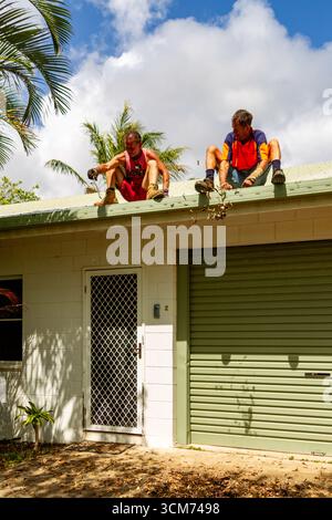 feuilles pile sol deux hommes toit assis nettoyage gouttières un homme au-dessus de la porte un au-dessus du toit de la porte de garage nettoyage des gouttières de toit des feuilles de débris Banque D'Images