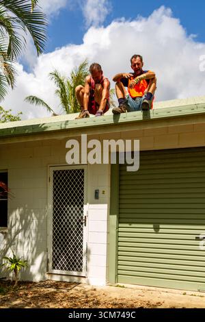 deux hommes dont un riant feuilles pile toit de sol assis nettoyage des gouttières un homme au-dessus de la porte un au-dessus du toit de la porte de garage nettoyage des gouttières de toit Banque D'Images