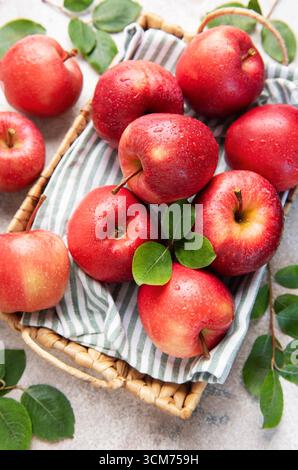 Pommes rouges mûres avec des gouttelettes d'eau se trouvent dans un panier en osier sur un chiffon rayé, incarnant la fraîcheur et une alimentation saine Banque D'Images