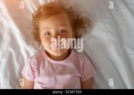 Mignon jeune fille allongée sur le linge de lit blanc portant t-shirt rose Banque D'Images