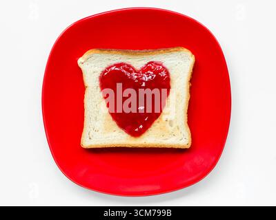 assiette rouge avec pain grillé et confiture en forme de coeur isolé sur blanc Banque D'Images