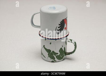 Deux tasses empilées en céramique, l'une blanche avec un motif rouge et l'autre verte avec des motifs d'éclaboussures, sur un fond clair Banque D'Images
