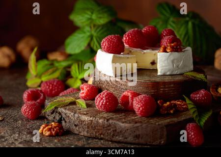 Camembert avec framboises fraîches et noix sur une table vintage brune. Banque D'Images