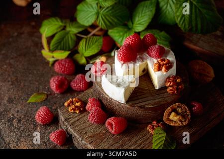 Camembert avec framboises fraîches et noix sur une table vintage brune. Banque D'Images