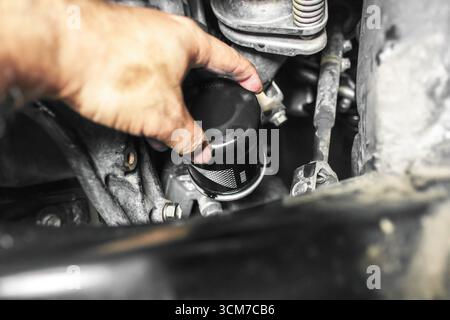 Main de mécanicien remplaçant le filtre à huile de voiture à l'intérieur du compartiment moteur, service d'entretien automobile, réparation de véhicule et entretien du moteur pour une performance lisse Banque D'Images