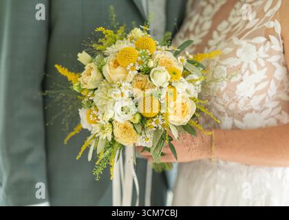 Beau bouquet de mariage avec des fleurs jaunes et blanches tenu par une mariée dans une robe délicate en dentelle. La disposition lumineuse complète l'environnement Banque D'Images