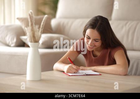 Femme heureuse prenant note dans l'agenda papier assis sur le sol dans le salon Banque D'Images
