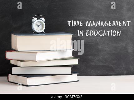 Réveil placé sur une pile de livres avec un tableau noir en arrière-plan avec le texte gestion du temps dans l'éducation écrit dessus Banque D'Images
