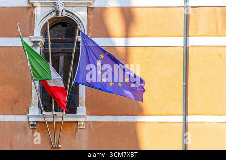 Drapeaux de l'Union européenne et de l'Italie sur la construction. Gros plan des drapeaux de l'Union européenne et de l'Italie agitant à l'extérieur d'un vieux bâtiment avec une fenêtre décorative et Banque D'Images