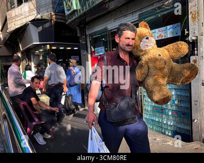 Téhéran, Iran. Un homme porte un grand ours en peluche sur son épaule tout en marchant dans une rue animée de la capitale. Banque D'Images