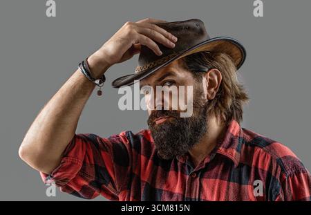 Chapeau de cow-boy en cuir. Beau jeune homme ajustant son chapeau de cow-boy. Homme non rasé cow-boys. Cow-boy américain. Style cow-boy dans une chemise à carreaux Banque D'Images