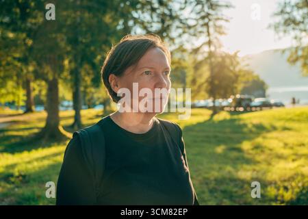 Portrait d'une femme brune mature détendue marchant à travers le parc au coucher du soleil d'été. Mise au point sélective. Banque D'Images