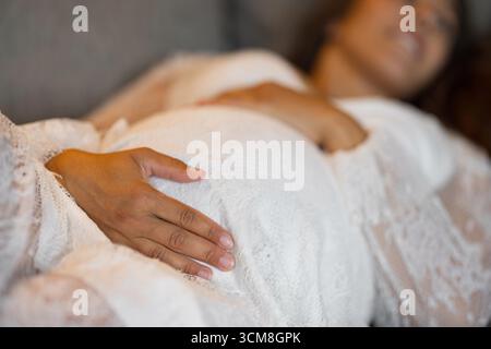 Une image sereine en gros plan d'une femme enceinte portant une dentelle blanche délicate, posant doucement ses mains sur son ventre, symbolisant l'amour maternel, l'anticipation Banque D'Images