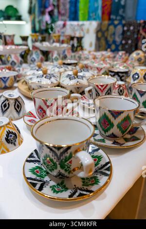 Tasses, soucoupes et bols colorés en céramique d'Asie centrale avec des motifs complexes et des accents dorés, disposés sur une surface blanche pour l'affichage Banque D'Images