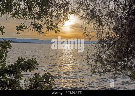 Coucher de soleil panoramique sur la mer Adriatique encadrée par des branches et la côte sur l'île de Krk Croatie Banque D'Images