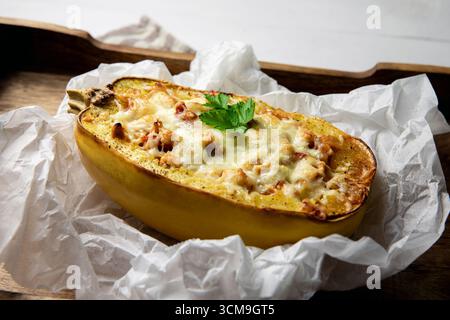 Vue de côté de courge spaghetti ou spaghetti végétal farci à la viande hachée et au fromage, servi dans sa coquille. Plat fait maison sur un bois rustique. Banque D'Images