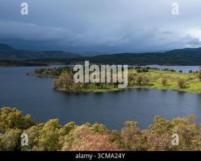 Eaux tranquilles du réservoir gabriel y Galán reflétant un ciel orageux, entourées d'une végétation luxuriante et de collines ondulantes en estrémadure, espagne Banque D'Images