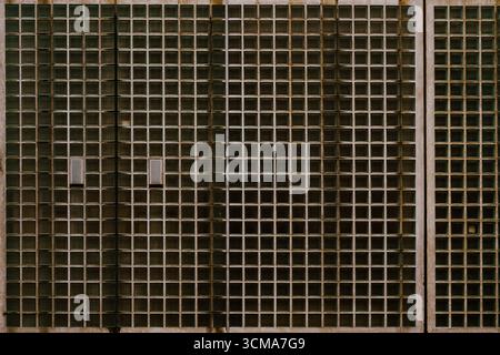 Sérénité géométrique : façade en verre givré cette ancienne façade en verre givré à Maastricht présente un motif géométrique serein mais frappant, composé d'innombrables carrés qui forment une grille sans couture sur la surface de la structure. Chaque carré capture la lumière différemment, créant une mosaïque subtile de nuances qui changent avec la lumière du jour changeante. Banque D'Images